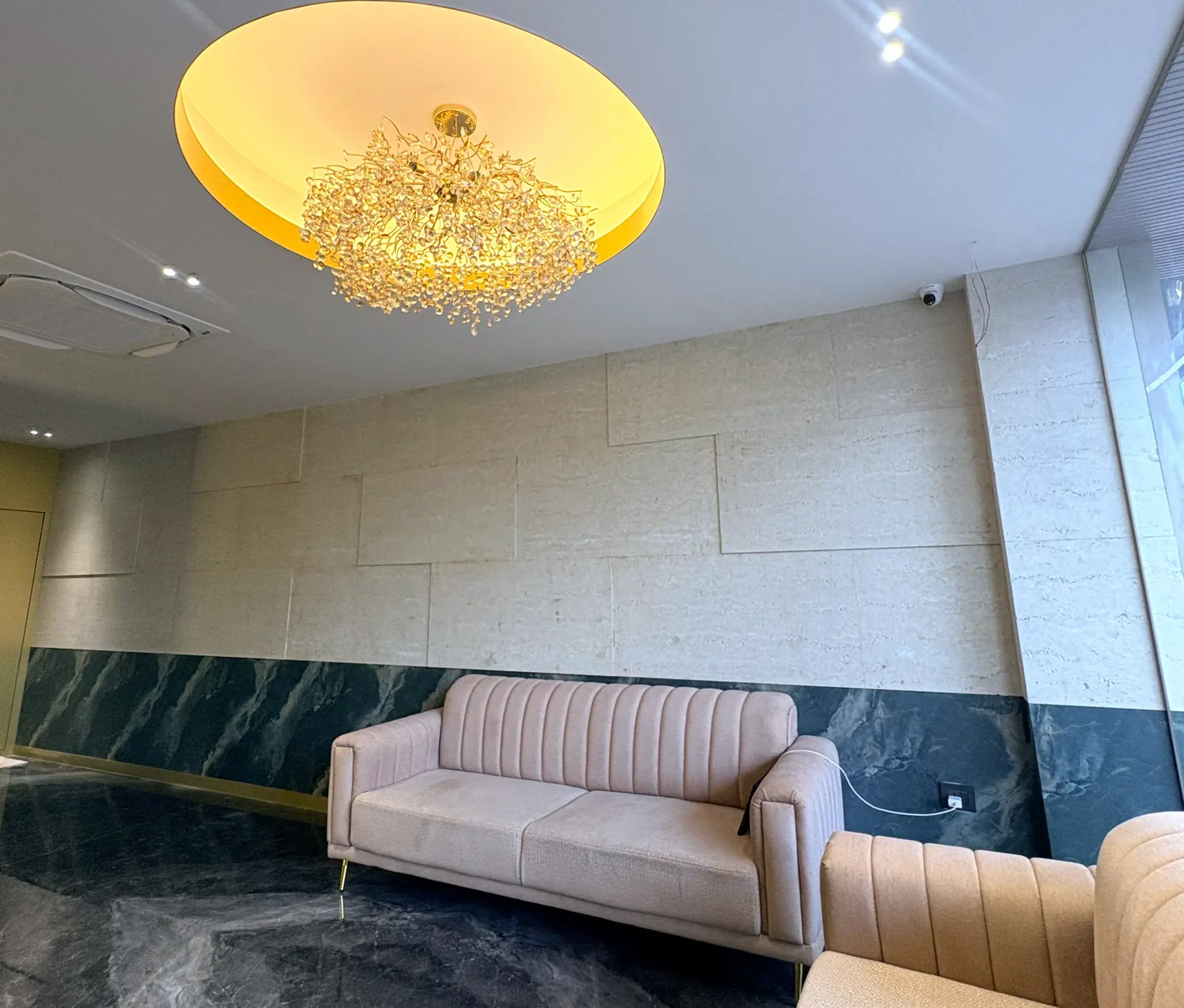 Lobby lounge with a cream sofa beneath a brass chandelier and travertine walls
