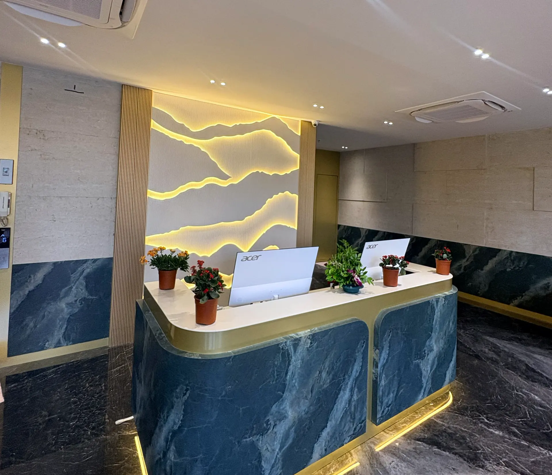 Reception desk in green marble with brass trim, beneath a backlit relief wall